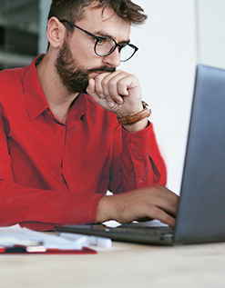 Mann sitzt vor Laptop und wirkt nachdenklich